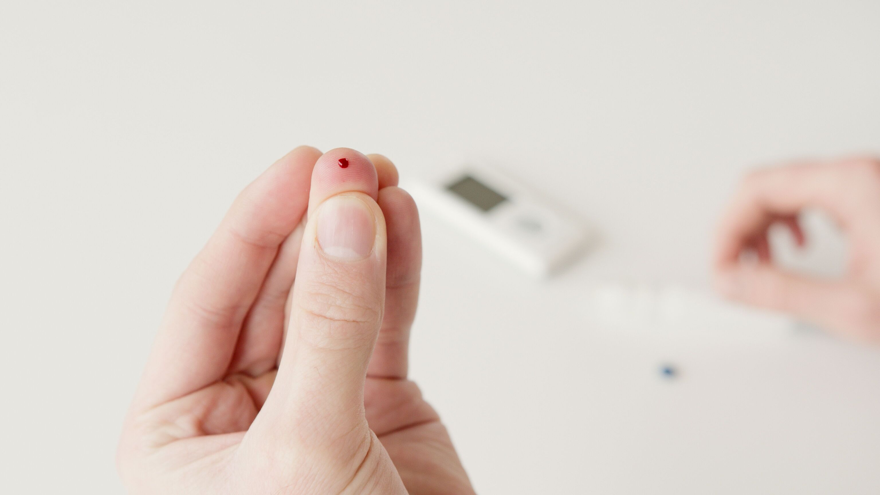 A fingertip with a small drop of blood next to a home glucose meter