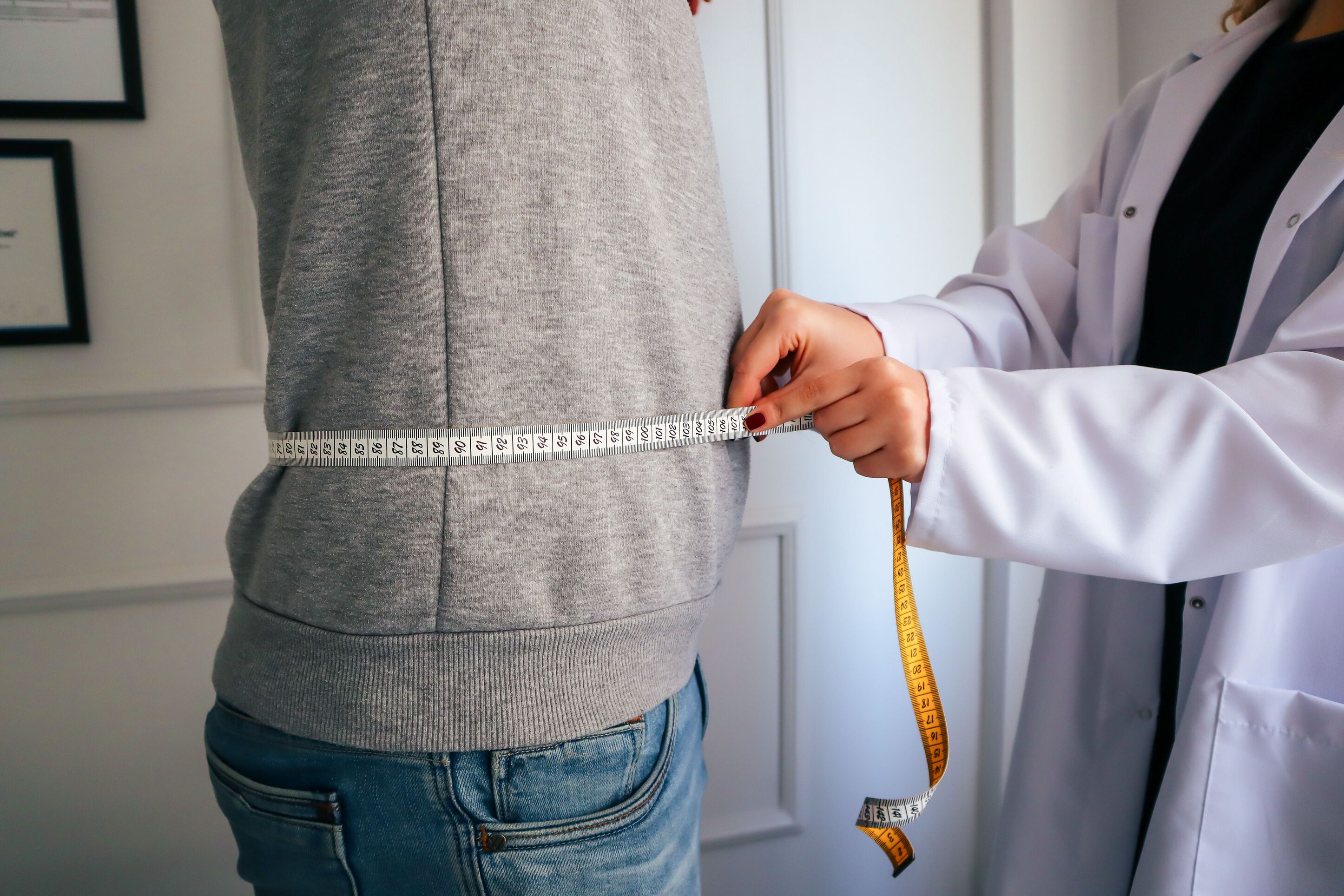 A tape measure wrapped around a man's waist over a grey sweater